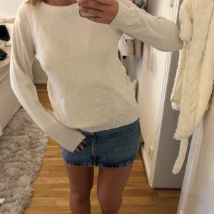 Vit stickad tröja med rund hals - Enkel och stilren vit stickad tröja med rund halsringning och ribbade muddar vid ärmslut och nederkant. Långärmad modell som är perfekt att matcha med jeans eller kjol för en clean look.