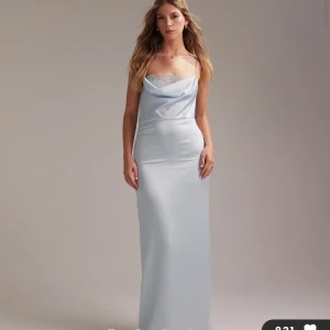 Ljusblå långklänning med spetsdetalj - Supersnygg ljusblå långklänning i satinliknande material med tunna axelband och vacker spetskant vid både bysten och ryggen. Klänningen har en draperad urringning fram och bak. Aldrig använd💗Skriv för fler bilder, priset går att förhandla