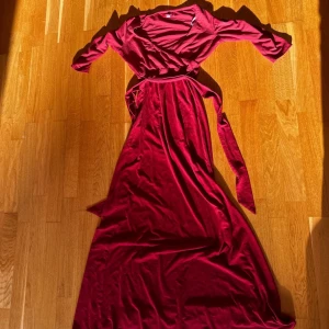 Röd omlottklänning från Guess - Säljer en röd lång omlottklänning från Guess i mjuk polyester. Klänningen har långa ärmar, knytband i midjan och en elegant v-ringning. Perfekt för dig som vill ha en stilren och bekväm look med lite extra längd.