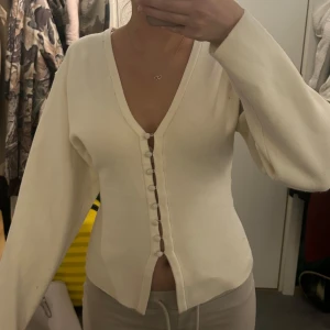 Krämvit kofta med knappar - Säljer en krämvit kofta med v-ringning och dekorativa knappar framtill. Från Gina. Nyskick.