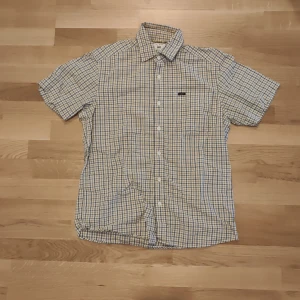 Rutig kortärmad skjorta från Lee - Kortärmad skjorta från Lee i ett blått och vitt rutigt mönster. Klassisk krage och knäppning framtill, samt en liten broderad logotyp på bröstet