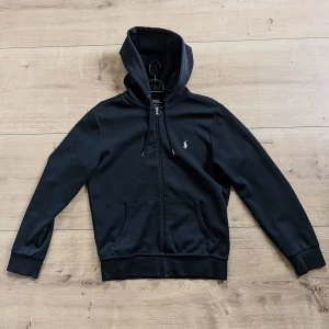 Svart hoodie från Polo Ralph Lauren - Svart hoodie med dragkedja från Polo Ralph Lauren. Klassisk design med broderad logga på bröstet, huva och fickor framtill. Perfekt för en avslappnad och stilren look. Ny pris ligger på runt 2300kr. Kvitto finns btw. Öppen för frågor!