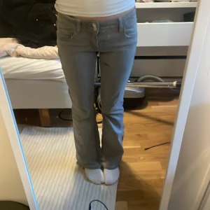Grå bootcut jeans med låg midja - Säljer ett par grå jeans med bootcut-modell och låg midja. Byxorna har klassisk femficksdesign och stängs med dragkedja och knapp. Perfekta för dig som gillar en avslappnad men ändå snygg look.