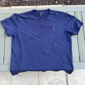 Marinblå t-shirt från Polo Ralph Lauren - Säljer nu en snygg marinblå t-shirt från Polo Ralph Lauren i bomull med klassisk röd broderad logga på bröstet. T-shirten har rund halsringning och korta ärmar, perfekt för en clean och stilren look. Skriv om du har frågor 🙏