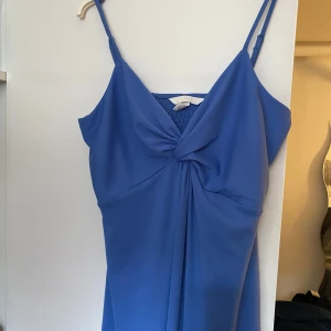 Blå långklänning med knut framtill från H&M - Säljer en blå långklänning från H&M med smala axelband och snygg knutdetalj framtill. Klänningen har v-ringning och är perfekt för sommarens tillfällen! Kontakta för frågor och prisförslag!