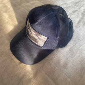 Manchuns velvet keps - Snygg mörkblå keps från med mesh på sidorna och baksidan för extra ventilation. Framsidan har en cool patch med svartvit bild på en sportbil. Justerbar baktill för perfekt passform. Perfekt accessoar för en sportig och trendig look.