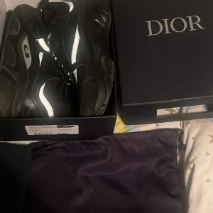 Svarta Dior sneakers med reflexdetaljer - Säljer ett par svarta Dior sneakers med feta vita reflexdetaljer och chunky sula. Skorna har snörning och är tillverkade i en mix av skinn och syntet. Kommer med originalkartong, dustbag och äkthetsbevis. Riktigt lyxiga och trendiga sneakers för dig som vill sticka ut.