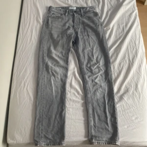 Gråa relaxed jeans från Jack & Jones - Snygga ljusgrå jeans från Jack & Jones i modellen Relaxed/Chris. Jeansen har en avslappnad passform med raka ben och klassiska fem fickor. Tillverkade i bomull med jeanskänsla och har bälteshällor och knappgylf. 