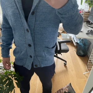 Ljusblå kofta från Gap - Säljer en ljusblå kofta från Gap i 100% bomull. Koftan har knappar framtill, två fickor och ribbade muddar vid ärmslut och nederkant. Perfekt för lager-på-lager och enkel att matcha med olika outfits.