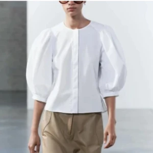 Vit blus med puffärmar - Säljer en stilren vit blus med rund halsringning och trendiga puffärmar i trekvarts längd. Blusen har en rak passform och är tillverkad i ett slätt bomullstyg som ger en fräsch och clean look. Perfekt för dig som gillar minimalistisk stil.