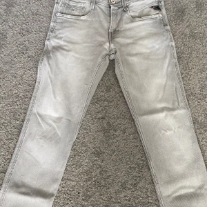 Ljusgrå Replay Anbass jeans - Säljer ett par ljusgrå Replay Anbass jeans med klassisk femficksdesign och raka ben. Jeansen har dragkedja och knapp i midjan samt diskret Replay-logga på fickan. Perfekta för dig som gillar stilrena och bekväma jeans. Storlek 29/32 modellen är 169 lång väger 55kg