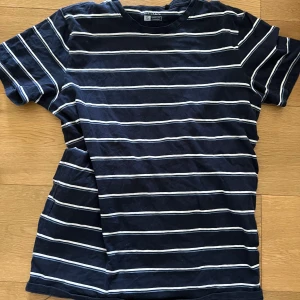 Mörkblå randig t-shirt från ETREL - Säljer en mörkblå t-shirt från ETREL med vita horisontella ränder. Klassisk passform och rund halsringning. Perfekt för en avslappnad stil och enkel att matcha med jeans eller shorts.