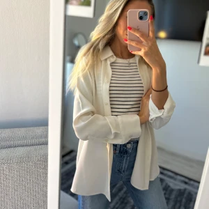 Vit långärmad skjorta från Zara - Klassisk vit skjorta från Zara i storlek XS. Skjortan har lång ärm, knappar framtill och en stilren krage. Tillverkad i ett mjukt och lätt material som ger en elegant känsla.