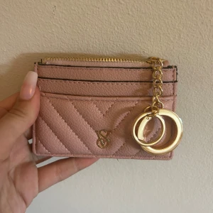 Rosa plånbok från Victoria's Secret - Supersöt rosa plånbok från Victoria's Secret med quiltad framsida och guldfärgade detaljer. Plånboken har dragkedja upptill, flera kortfack och en snygg kedja. Perfekt storlek för att ha med sig överallt. Köpt i London för 300, säljer för 200 då den aldrig är använd!