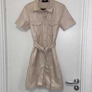 Beige skjort klänning i skinnlook Bik Bok XS - Jag har använt denna max 3 ggr, så den är i jättebra skick! 🫶  🔹 Ljusrosa/beige ton (lite olika beroende på ljuset) 🔹 Lädermaterial 🔹 Knappar hela vägen + midjebälte 🔹 Perfekt till både vardag och utekvällar!  Köpt för ett par år sen, men har mest hängt i garderoben.