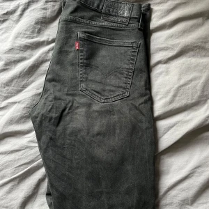 Levi's 511 svarta jeans W32 L34 - Svarta Levi's 511 jeans med klassisk femficksdesign och rakt snitt. Jeansen har en mörk tvätt och är tillverkade i mjukt denim. Perfekta för dig som gillar en stilren look med lite edge. Levi's patch bak i midjan och röd logga på bakfickan.