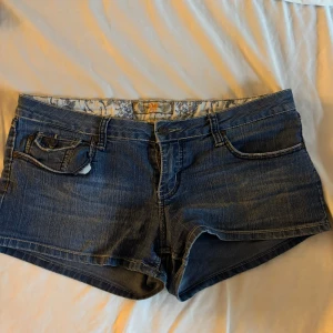 Blå jeansshorts från YMI Jeans - Säljer ett par klassiska blå jeansshorts från YMI Jeans med snygga bakfickor och låg midja. Shortsen har en normal passform och är tillverkade i en bomulls- och polyestermix med lite stretch för extra komfort.