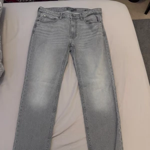 Grå jeansbyxor från Dressman - Säljer ett par grå jeansbyxor från Dressman med klassisk femficksdesign och normal passform. Byxorna har dragkedja och knapp i midjan samt raka ben. Perfekta för en stilren vardagslook. Storlek W32/L30