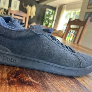 Mörkblå sneakers från Polo Ralph Lauren - Säljer ett par mörkblå sneakers från Polo Ralph Lauren i mocka med klassisk snörning och rund tå. Skorna har en diskret logga på sidan och Polo-märke på plösen. Perfekta för en stilren och avslappnad look.