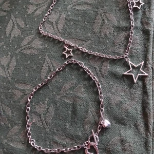 Silverfärgade halsband med stjärnor och hjärtan  - Säljer ett set med halsband i silverfärgad metall. Halsbanden har kedja med stjärnberlocker i olika storlekar, medan det andea har en hjärtformad toggle-låsning och en liten hjärtberlock. Perfekt för dig som gillar detaljer och coola smycken.