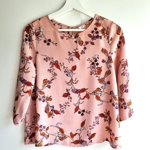 Blommig rosa blus Cubus - Supersöt blus i ljusrosa från Cubus med blommigt mönster i lila, orange och vitt. Modellen har trekvartsärm, rund hals och dragkedja bak. Perfekt för dig som gillar romantiska vibes och färg.