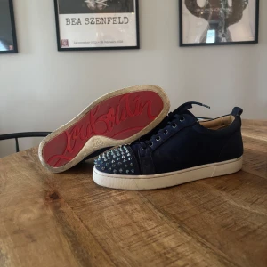 Mörkblå sneakers med nitar och röd sula från Christian Louboutin - Säljer ett par mörkblå sneakers från Christian Louboutin med nitar, använda ett fåtal gången men fortfarande i riktigt bra skick! Extremt stilrena och snygga, storlek 42 men extremt stora i storlek så passar mig som har 43/44