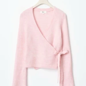 Ljusrosa omlottkofta med knyt - Superfin ljusrosa omlottkofta med knyt i sidan. Tröjan har lång ärm och är croppad i modellen, perfekt att styla över ett linne eller klänning. Mjuk och skön, passar till många olika outfits.