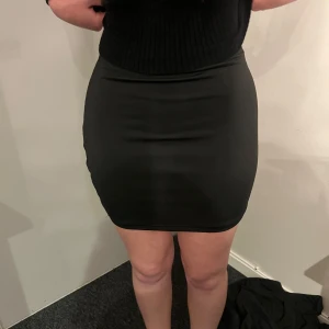 Svart tight kjol - Enkel och stilren svart tight kjol i kort modell. Kjolen har en slät yta utan synliga detaljer och passar perfekt till många olika outfits. Materialet känns stretchigt och följsamt.