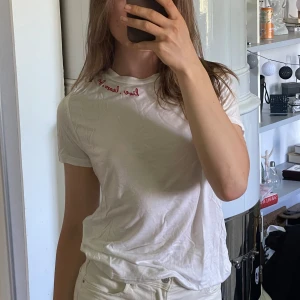 Vit t-shirt med röd brodyr från Divided - Vit t-shirt från Divided med röd broderad text 'live. learn. love' vid halsringningen. Klassisk passform och rund hals. Perfekt basic med en liten detalj som sticker ut. Söt och lätt, perfekt nu till sommaren.