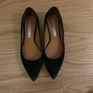 Svarta ballerinaskor i mocka - Snygga svarta ballerinaskor från Other Stories i mjuk mocka. Skorna har spetsig tå och låg klack, vilket ger en stilren och modern look. Perfekta att matcha med både jeans och klänning för en trendig vibe. Enda defekten dessa har är att det är vissa nötningar i lädret (se bild 4 för exempel) , annars är de jätte fräscha och i bra skick. Nypris - över 1000kr, säljer för 400kr