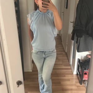 Ljusblå blus med volangkrage - Säljer en ljusblå blus med volangdetalj vid halsen och ärmlös design. Blusen har en lös passform och är tillverkad i ett tunt, luftigt material som passar perfekt till sommaren. 💌 köparen står för frakten