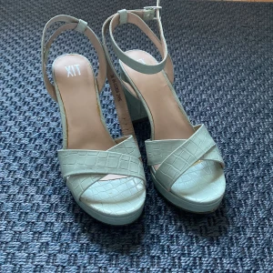 Ljusa gröna klackskor - Snygga ljusgröna klackskor och öppen tå från XIT. De har ett krokodilmönster och justerbart spänne runt ankeln. Perfekta för att ge en stilren touch till din outfit. Kommer aldrig till användning och använt en gång. 🩷🩷