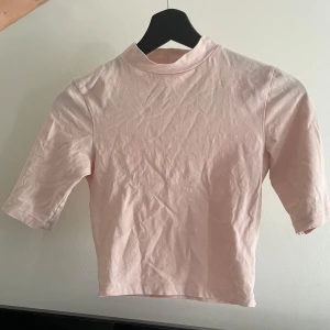 Ljusrosa polotopp från ASOS - Säljer en ljusrosa polotopp från ASOS med trekvartsärm. Perfekt för en stilren och enkel look. Toppen är i ett mjukt material som känns skönt mot huden.