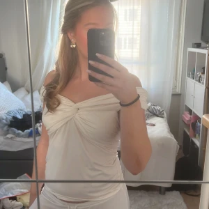 Vit axelbandslös topp - Säljer en stilren vit axelbandslös topp med knytdetalj framtill. Perfekt för sommarens varma dagar eller en kväll ute. Toppen har en elegant och enkel design som passar till många olika tillfällen.
