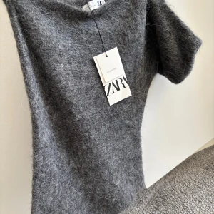 Grå tröja från Zara - Säljer en stilren grå tröja från Zara. Den är mjuk och har en fluffig textur som ger en lyxig känsla.  One of shoulder aldrig använd från Zara 