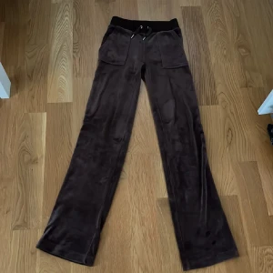 Bruna mjukisbyxor från Juicy Couture str XXS men passar även XS - Säljer ett par bruna mjukisbyxor från Juicy Couture i str XXS men passar även XS. Byxorna har en bekväm passform med snörning i midjan och praktiska fickor både fram och bak. Perfekta för en avslappnad stil. Använda få gånger.