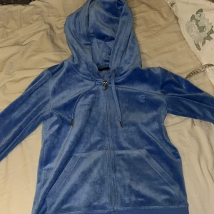 Blå velourjacka från Juicy Couture - Säljer en snygg blå velourjacka från Juicy Couture med dragkedja och huva. Jackan har långa ärmar och ribbade muddar. Perfekt för en avslappnad och stilren look. 💙 På sista bilden ser man en liten liten fläck som inte syns men försvinner i tvätten, tvättas innan jag skickar💕