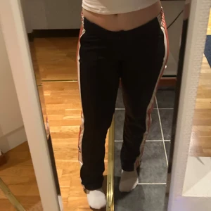 Adidasbyxor - Adidasbyxor med knappar längs benen, går att öppna alla knappar. Mellanhög midja med raka ben, en missfärgning på ena höften. 