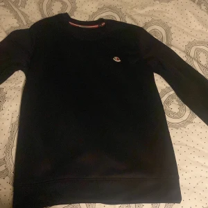 Svart tröja från Moncler - Snygg svart tröja från Moncler med rund hals och liten logga på bröstet. Perfekt för en stilren look. Passar till både jeans och chinos. Helt ny!