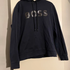 Mörkblå hoodie från BOSS - Säljer en snygg mörkblå hoodie från BOSS i storlek s med stor logga på bröstet. Tröjan har långa ärmar.