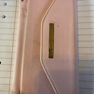 Rosa plånbok med gulddetaljer - Snygg rosa plånbok med guldfärgad logotyp på framsidan. Plånboken har flera kortfack och en praktisk design som även fungerar som mobilfodral. Perfekt för att hålla ordning på dina kort och mobilen i en stilren förpackning.