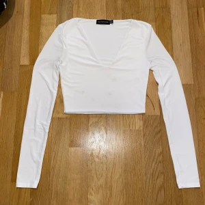 Vit långärmad topp från PrettyLittleThing - Säljer en stilren vit långärmad topp från PrettyLittleThing. Toppen har en v-ringad design och är perfekt för en chic och enkel look. Passar bra till både jeans och kjol. Den fick några små fläckar efter jag hade tvättat den, så är osäker om det går bort eller inte, köpte den för 249kr