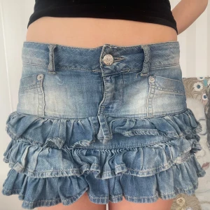 Blå jeanskjol med volanger - Snygg vintage lågmidjad jeanskjol. Midjemått 40, längd 30