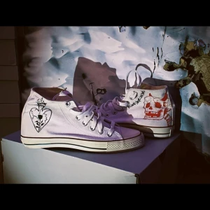 Vita sneakers med tryck från Converse - Unika vita Converse sneakers med handritade motiv av hjärtan och dödskallar. Klassisk hög modell med snörning och rund tå. Perfekta för att ge din stil en personlig touch.