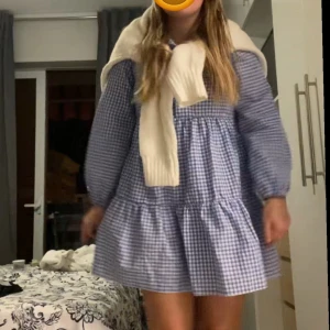 Blå och vit rutig klänning - Blå och vit rutig klänning med långa ärmar och knappar framtill. Klänningen har en luftig passform och volanger som ger en söt och avslappnad look. Perfekt för vår och sommar!🤩