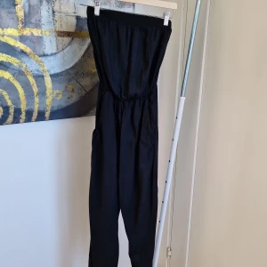 Svarta armlös jumpsuit med resårmidja - Säljer svarta jumpsuit. har en loose passform och är tillverkade i ett mjukt material som ger en bekväm känsla. Perfekta för en avslappnad stil.