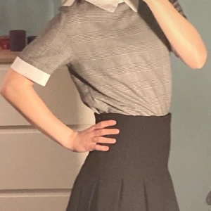 Grå rutig blus med vit krage - Snygg grå rutig blus med vit krage och korta ärmar. Perfekt för en stilren look. Passar bra till både kjol och byxor.