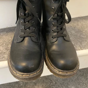 Svarta boots från Rieker - Säljer ett par svarta boots från Rieker med snörning och dragkedja på sidan. Skorna har en robust sula och rund tå, vilket gör dem perfekta för både stil och komfort. Perfekt för höst- och vinterdagar.