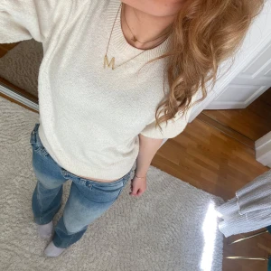 Beige stickad tröja - Säljer en stilren beige stickad tröja med korta ärmar och ribbade detaljer vid ärmslut och nederkant. Perfekt för en avslappnad och chic look.