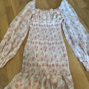 Blommig klänning med långa ärmar - Söt blommig klänning med smockdetaljer och långa ärmar. 